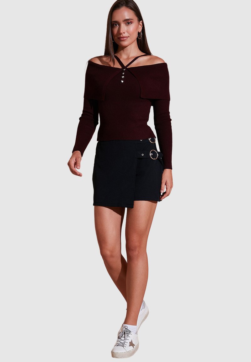 Burgundi off-shoulder dryžuotas marškinėlis su mygtukų detale, derinamas su juoda apvyniota sijonu, kurio šonuose yra kišenės ir metalinės detalės. Baltos sportbačiai.