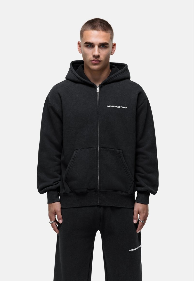 Felpa nera con zip realizzata in tessuto morbido, caratterizzata da una grande tasca frontale e dalla scritta "GOODFORNOTHING" in bianco sul petto.