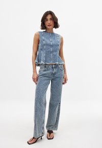 Blå denim tvådelat set bestående av en ärmlös topp med peplumkant och högmidjade, vida byxor. Förstörda kanter är synliga.