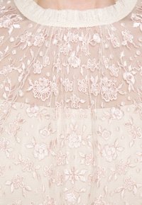 Tissu en dentelle florale délicate rose clair avec des fleurs brodées couvrant une partie supérieure transparente du vêtement et le décolleté.