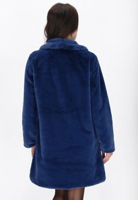 Mørkeblå faux fur frakke med krave og lange ærmer, der har en blød tekstur og knælang silhuet. Bagvenden viser ingen yderligere detaljer.