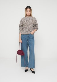 Pulover tricotat texturat, multicolor, cu decolteu rotund, asortat cu blugi din denim negru cu picioare late și o mică geantă de mână maroniu cu șnur.