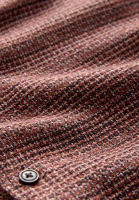 Suure tähelepanuga pruun ja must houndstooth kangas koos tekstuuri ja ühe tumeda nööbiga õmmelduna vasakus alumises servas.