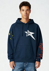 Sweat à capuche bleu marine en mélange de coton avec une poche avant. Présente un graphisme d'étoile blanche sur la poitrine et des accents d'étoile rouges sur la manche.