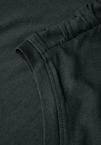 Tissu vert foncé avec une texture douce. Présente un poignet roulé et une couture lisse. Convient pour un usage décontracté.