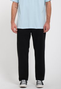 Zwarte broek met een ontspannen pasvorm en rechte pijpen, gecombineerd met een lichtblauw T-shirt en zwart-witte sneakers. Zacht katoen materiaal.