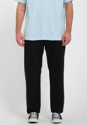 Zwarte broek met een ontspannen pasvorm en rechte pijpen, gecombineerd met een lichtblauw T-shirt en zwart-witte sneakers. Zacht katoen materiaal.