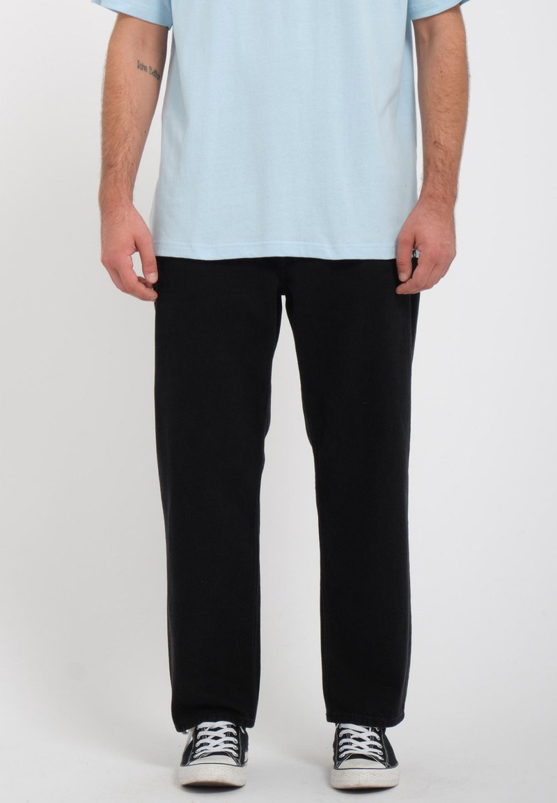Pantaloni neri con una vestibilità comoda e gamba dritta, abbinati a una maglietta azzurra chiara e sneakers bianco e nero. Materiale di cotone morbido.