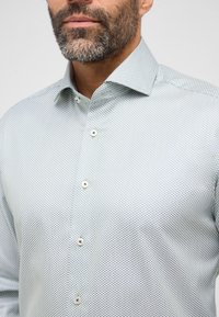 Lichtgroen geruite shirt van stof met een gestructureerd patroon. Beschikt over een klassieke kraag en een knoopsluiting met contrasterende knopen.