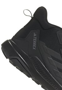 Sort sportsko med en tekstureret mesh-overdel, forstærket hæl og gummisål. Har en pull-tab og diskret logo-detaljering.