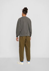 Felpa grigia oversize con polsini e orlo a coste, abbinata a pantaloni cargo color oliva con tasche laterali e un'etichetta con logo. Sneakers bianche casual.