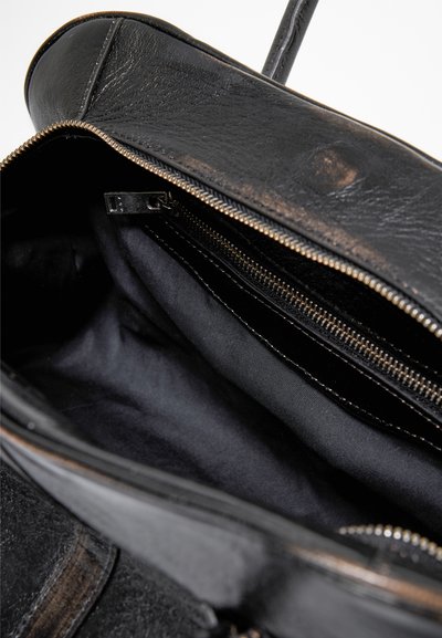 Interno di una borsa in pelle nera con due scomparti con zip, foderata in tessuto morbido di colore scuro e con hardware dorato. È visibile una finitura esterna testurizzata.