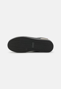 Black rubber sole featuring a zigzag pattern for traction, with a smooth, round shape and a flat surface. Notable rectangular logo accent.
