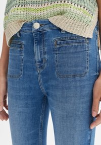 Jeans de mezclilla azul claro con un diseño ajustado, que presentan costuras doradas, bolsillos traseros y cierre de botón en la cintura.