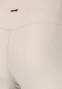 Leggings beige chiaro realizzati in un tessuto morbido ed elastico, con delicati dettagli di cucitura e un piccolo logo metallico sul cinturino.