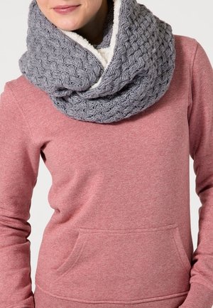 Femme portant une épaisse écharpe infinity en maille grise doublée en polaire et un pull à manches longues rose avec une poche avant.