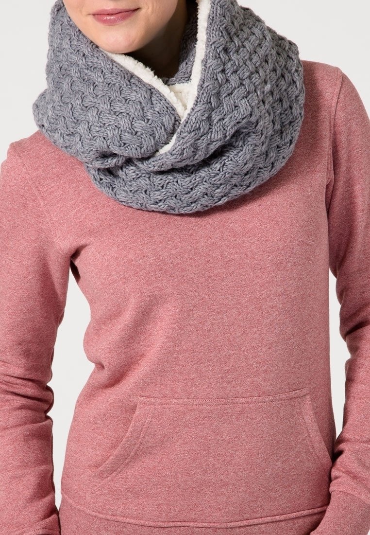 Femme portant une épaisse écharpe infinity en maille grise doublée en polaire et un pull à manches longues rose avec une poche avant.