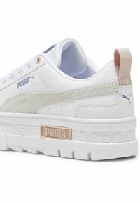 White sneaker with a smooth leather upper, light beige accents, textured stitching, and a chunky white sole featuring a logo at the heel.
