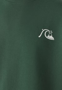 Sweatshirt vert foncé avec un col rond, présentant un design graphique blanc d'une vague et d'une montagne. Fabriqué à partir d'un tissu doux et texturé.