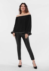 Svart off-shoulder topp med volanger, kombinert med glinsende svarte fake skinnbukser og svarte høye hæler.