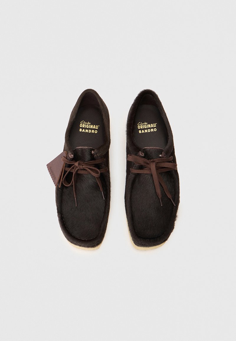 Brown fur slip-on shoes with a rounded shape, featuring dark laces and a beige rubber sole. Branding visible on the insole.