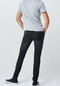 Jeans skinny negros con cinco bolsillos, combinados con una camiseta gris y zapatillas negras de caña alta. Textura suave con detalles mínimos.