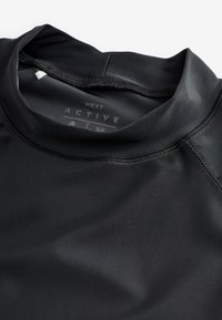 Schwarzes Sportoberteil aus glattem, dehnbarem Stoff. Verfügt über einen hohen Kragen und Flatlock-Nähte für Komfort und Langlebigkeit.