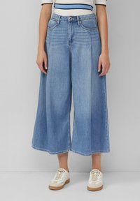 Lichtblauwe denim culottes met een losse, brede pasvorm, voorzien van frontzakken en een knoopsluiting. Gestyleerd met witte sneakers.