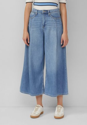 Light blue denim culottes with a loose, wide-leg design, featuring front pockets and a button closure. Styled with white sneakers.