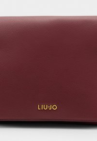 Burgundská kožená taška s texturovaným povrchem a zlatým logem "LIUJO" na přední straně. Obdélníkový tvar s prošívanými okraji.