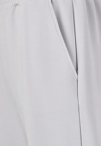 Lichtgrijze sportbroek gemaakt van zacht, rekbaar materiaal met zijzakken en een geplooide tailleband, met een gladde textuur.