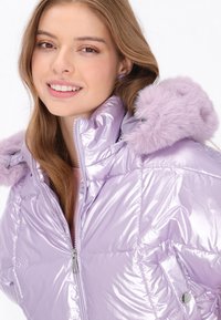 Błyszcząca, jasnofioletowa kurtka puchowa z zapięciem na zamek, dużym kołnierzem oraz odpinanym kapturem z sztucznego futra. Posiada przeszywane panele i kieszenie na zatrzaski.