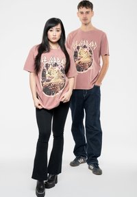 Two models wear oversized graphic t-shirts in faded pink with a leopard design. The woman pairs her shirt with black flared pants and heeled boots.