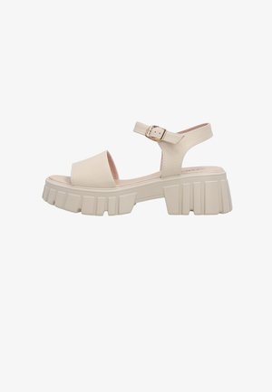 Beige chunky platform sandal with wide front strap and adjustable ankle strap featuring a gold buckle.