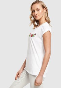 Hvid t-shirt med korte ærmer og omviklede manchetter, prydet med farverig broderi med ferietema. Stoffet virker blødt og har en afslappet pasform.