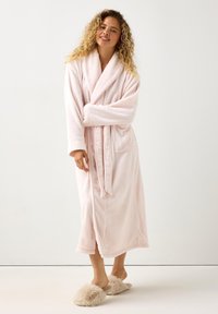 Soft pink, long plush bathrobe with a shawl collar, belted waist, and two side pockets. Paired with fluffy beige slippers.