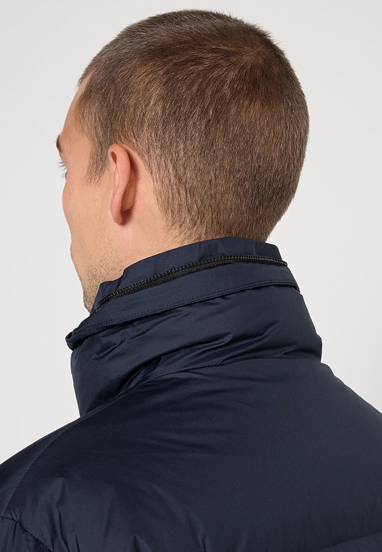 Marineblauer gepolsteter Mantel mit hohem Kragen und schwarzem Reißverschlussdetail. Glatte Textur und leichtes Material, von hinten gesehen.