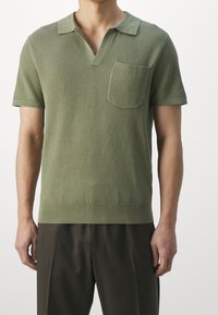 Neulotut vihreät poolopaidat, joissa on teksturoidun kuvioinnin, lyhyet hihat, V-aukko ja rintatasku. Viimeistelty resorilla helmassa.