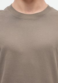 Close-up of a person wearing a plain brown crew neck t-shirt, showing neck and upper chest area.