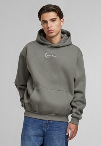 Felpa grigia con cappuccio e cordino, tasca frontale e logo bianco. Tessuto morbido e vestibilità comoda, abbinata a jeans blu.