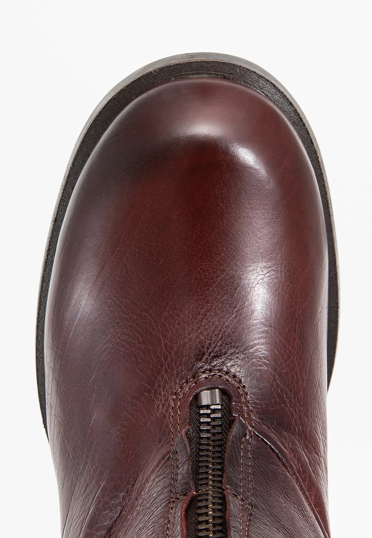 Botín de cuero marrón con punta redonda, cremallera lateral y acabado texturizado. La suela es de color contrastante y ligeramente elevada.