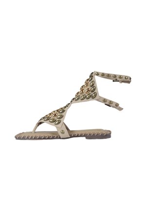 Sandalo basso beige con borchie ovali metalliche, cinturino alla caviglia e dettaglio intrecciato sul bordo della suola.