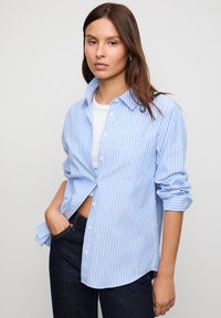Blue and white striped button-up shirt with a collar, single chest pocket, rolled sleeves, and a relaxed fit, made from lightweight fabric.
