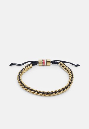 Bracciale in oro con accenti in tessuto blu navy, dotato di una chiusura centrale in metallo con strisce rosse e bianche. Realizzato con anelli intrecciati.