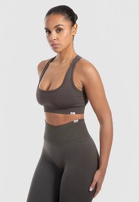 Sujetador deportivo y pantalones de cintura alta en verde oliva oscuro. Textura acanalada, diseño de soporte y detalle del logo en la banda.