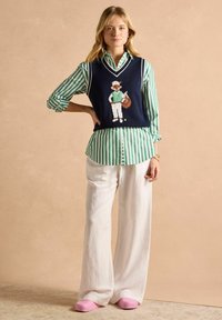 Tumes sinine kootud vest valgete äärtega, millel on rebane muster, kihtidega rohelise ja valge triibulise särgi kohal; koos laiad valged püksid ja roosad puuklikud.