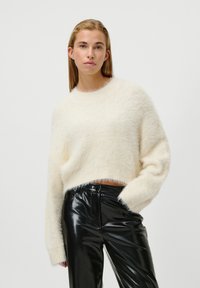Pull court couleur crème avec une texture douce, décolleté rond et manches longues. Associé à un pantalon noir en simili cuir, taille haute, brillant.