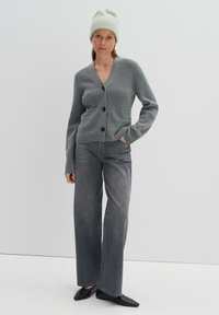 Cardigan grigio a maglia con scollo a V, tasca singola e bottoni neri, abbinato a jeans grigi a vita alta e ballerine nere a punta.