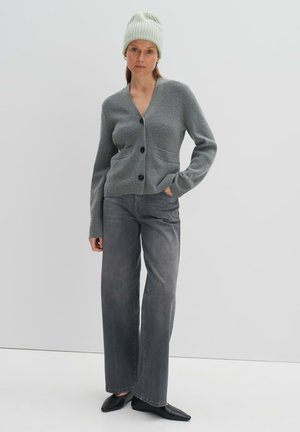 Grijze gebreide cardigan met een V-hals, een enkele zak en zwarte knopen, gecombineerd met hoogstaande grijze jeans en zwarte puntige flats.
