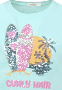 T-shirt azzurro chiaro con un design di paillettes che presenta due tavole da surf e palme, con il testo "CURLEY HAIR" in rosa sottostante.